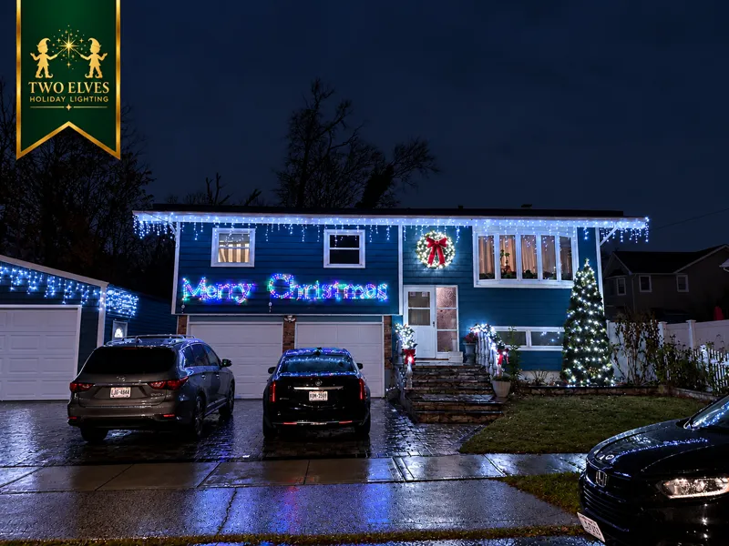 Blue home with icicle lights, multicolor Merry Christmas sign and lit tree