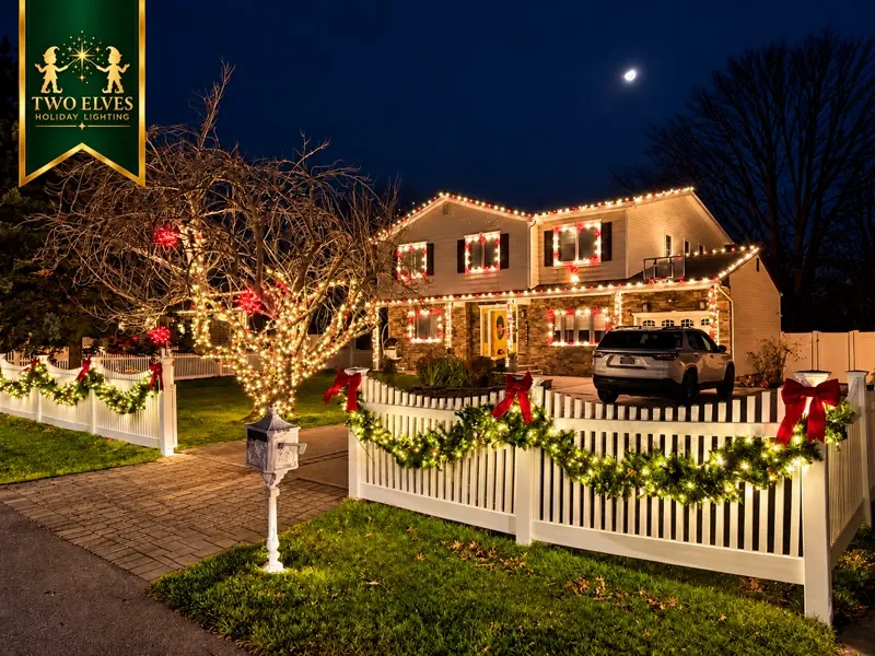 Fenced home with red-and-white lighting, lit tree and garland with bows